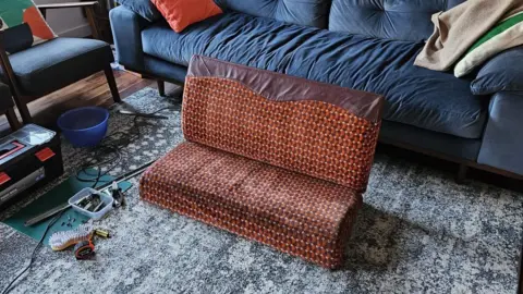 Matt McCallum A bright orange and red subway seat converted into a couch without armrests and legs in a living room.