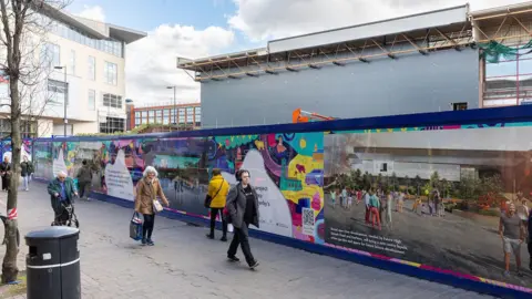 People milling about in front of a building site in Derby city centre