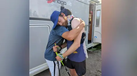 Richard Stennett Richard Stennett embracing a friend in front of a motorhome.