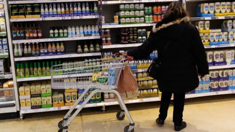 A woman photographed from behind in front of the sauce aisle deciding what to buy