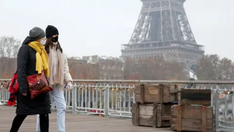 Getty Images Women walk in front of the Eiffel Tower wearing Covid face masks, November 2021