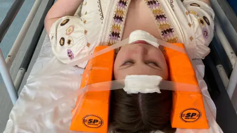 Johanna Dart Johanna lying on a hospital bed with neck brace on