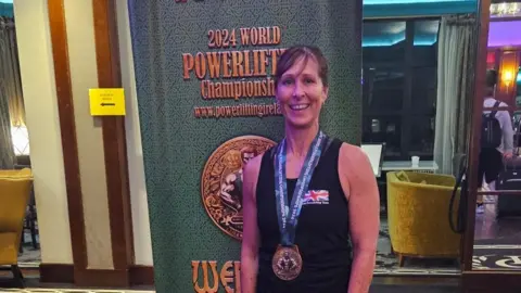 BBC Louise Clark smiling at the camera in a black tank top with a gold medal around her neck.