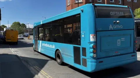 BBC A blue single-decker bus with the word Arriva on the back and arrivabus.co.uk on the side.
