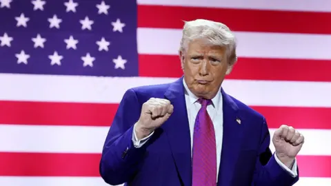 Getty Images US President Donald Trump pumps his fists on stage with an American flag seen behind him as he tours the Al Udeid Air Base on 15 May 2025, in Doha, Qatar.