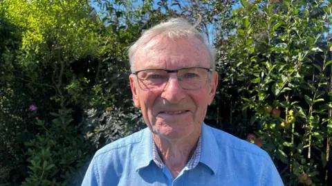 Man with grey hair, glasses, and a blue shirt