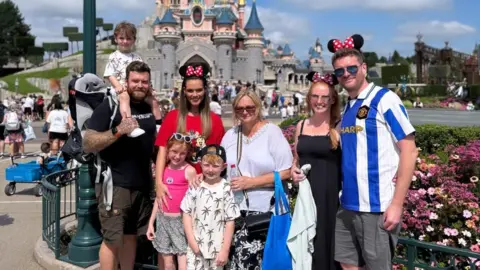 Family handout A group of people are standing in-front of a Disney castle wearing Mickey Mouse ears. Alison is in the middle. There are three young children, Alison’s grandchildren