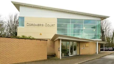 A large partially glass-fronted building with a 'coroners' court' sign.