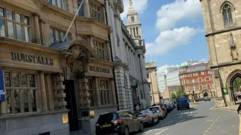 Lowgate in Hull's Old Town, with buildings made of old concrete stones and a view of the road with parked cars. 