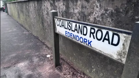 A concrete wall with the sign "Coalisland Road, Edendork'.