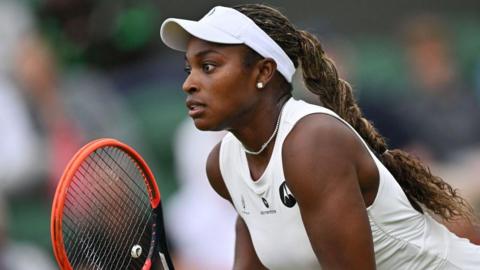 Sloane Stephens holds her racquet wearing a white dress as she prepares to return a serve