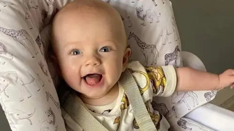 A baby boy smiles widely in a high chair