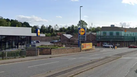A mostly empty road with two lanes on each side, and a Lidl supermarket in the background. 