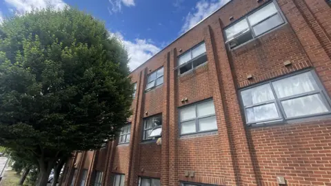 A three storey red brick building with trees in front of it.