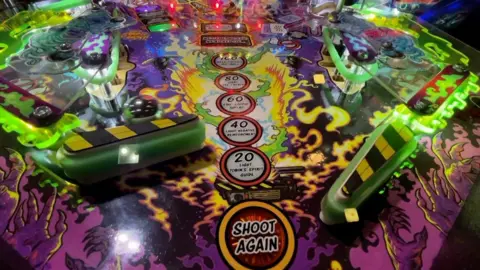 Close up of playing surface of pinball machine showing flippers and ball in play
