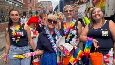 A group of women wearing rainbow Hawaiian leis and holding buckets