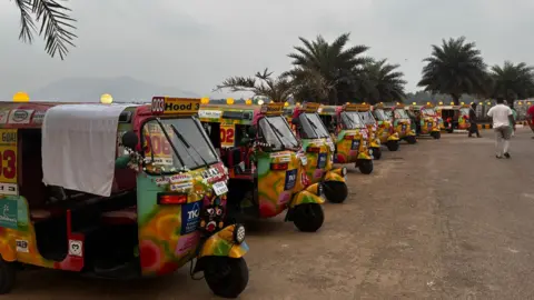 Rows of tuk-tuks parked. They are yellow and a lot of other vibrant colours 