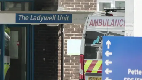 A view from outside the north Devon District Hospital maternity unit. There is a sign above the entrance which has the words 'The Ladywell Unit'. There is a blue sign with directions in the bottom right.