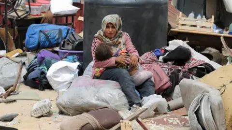 Woman sits with child as Palestinians flee Rafah due to Israeli military operation