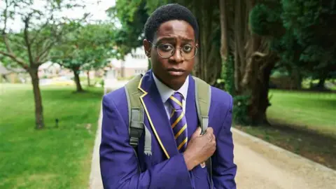 Myles Kamwendo as Omar on Boarders. He is wearing a royal blue school uniform walking down a path.