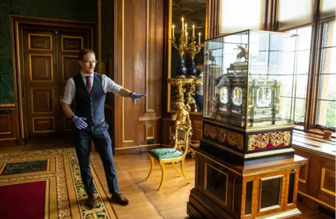 Antonio Olmos Fjodor gestures to a large organ clock in a state apartment