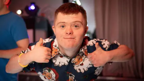 Family photo A man smiling at the camera giving a thumbs-up. He has a Santa shirt on.