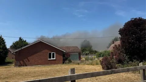 George King/BBC Smoke billows in the air from a fire. The fire is blocked from view due to a bungalow property. 