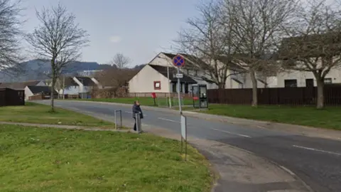 A view of an entrance to Golf View Road in Inverness. The street has rows of white-walled properties of different types.