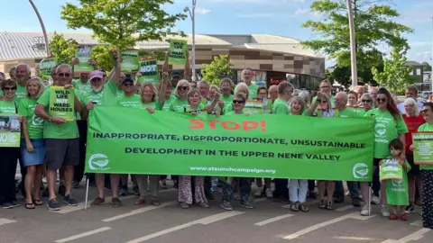 Staunch A large group of people standing holding a green banner. They are outside and are mostly wearing green T-shirts.