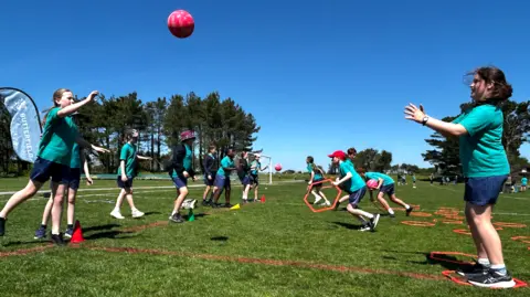 BBC Students playing netball in Jersey. They are wearing green and blue uniforms.
