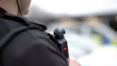 Devon and Cornwall Police Over the shoulder shot of police officer in dark uniform with a small camera on chest.