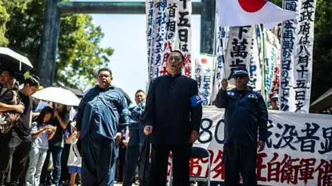 AFP Men in uniform holding banners and visitors shielding themselves with umbrellas to protect them from the heat in Tokyo on VJ Day 