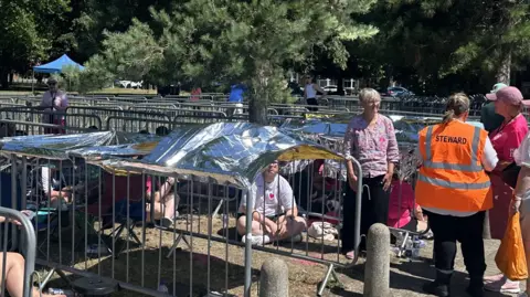 Alice Cunningham/BBC Fans sit on the ground within lines of metal gates with foil blankets resting above them to provide shade.