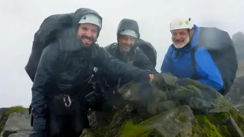 PA Media Three climbers on top of a mountain under a grey sky