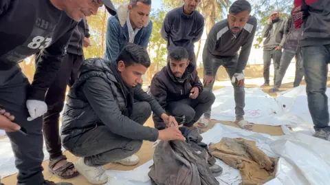 Young man leaning over clothes in white body bag