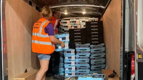 Towcester Community Larder A woman and a man load pallets of food into the back of a van.