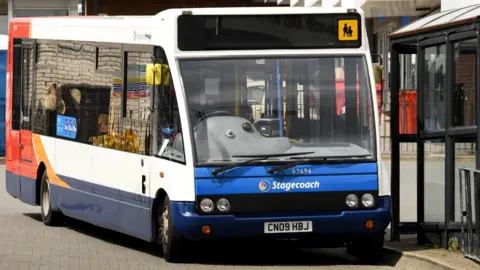 A Stagecoach bus in red, orange and blue livery parked next to a bus stop and shelter.