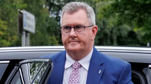 PA Media Donaldson wears glasses. He has a navy suit on with a fish pin attached. He's getting out of a car. 