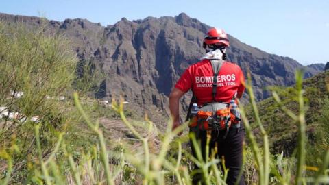 A firefighter searing near the village of Masca in northern Tenerife, a steep mountainside is visible in the bacground