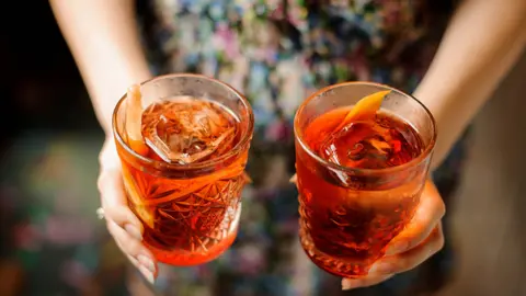 Getty Images Two hands carrying rum cocktails