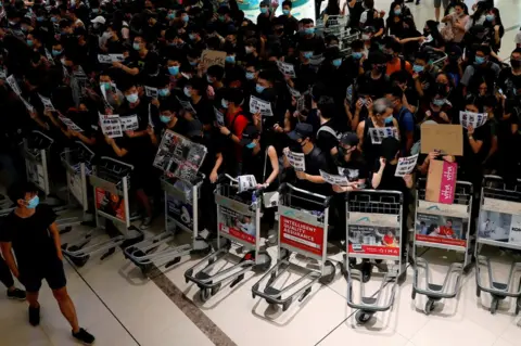 Reuters Anti-extradition bill protesters use trolleys to stop passengers from entering the security gates during a mass demonstration after a woman was shot in the eye, at the Hong Kong international airport, in Hong Kong China