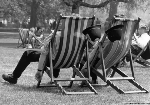 Evening Standard/Getty Images Two London policemen take the weight off their feet during the May heatwave, while patrolling in the park