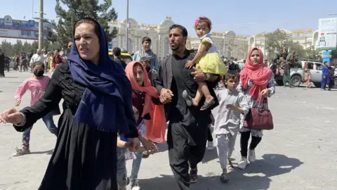 Getty Images Afghan family rushes to Kabul airport, on Monday