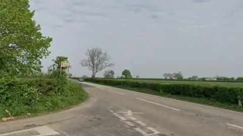 A road junction, showing the A39. It is a rural road, surrounded by green fields and trees. 