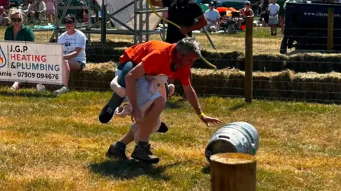 Frampton Fundraisers A man wearing a sheep outfit on his leg pushes a barrel.