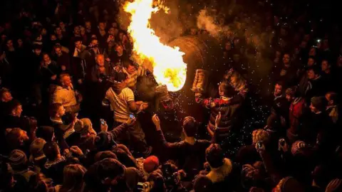 Getty Images A flaming tar barrel at the centre of a huge crowd of people. It is dark and the glow is lighting up everyone's faces