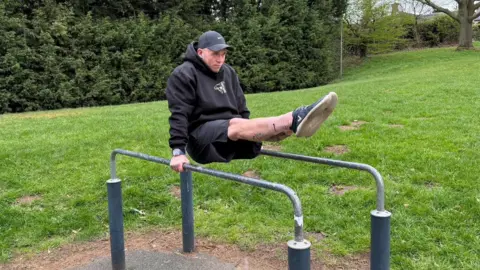 James placing his legs in the sky on a bar at an outdoor gym