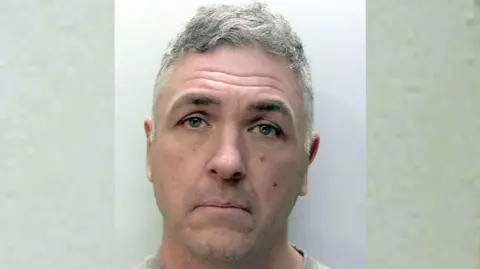 Close up of Paul Butler. Butler is looking into the camera. He is standing against a grey wall.
