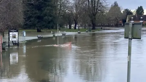 A road in Abingdon submerged under several inches of water. At the edge of the water are benches and bins.