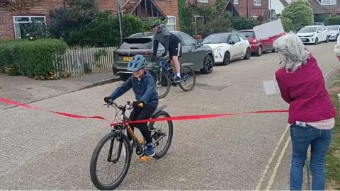 Carla A mon on a bike cycling through a red finish line ribbon.